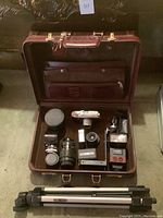 Assorted camera gear inside open briefcase including camera, lenses, flash, tripod
