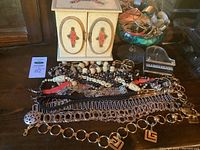 Overview of costume jewelry chain belts, necklaces, jewel box, and glass trinket bowl arranged on wooden surface