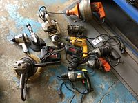 Multiple electric hand tools including various drills and tools laid out on a blue floor showing cords and tool handles.