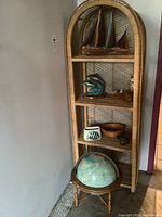 Full view of wicker shelf with ocean themed decorations including sailboats, dolphin figurine, vase, wooden bowl, sand, and globe at base.