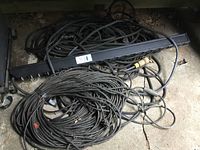 View of multiple heavy gauge black extension cords and a long black power strip with six outlets laid on a concrete floor.