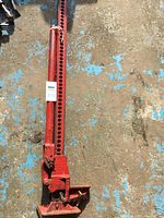 Full view of red heavy duty farm jack lying on ground showing length and lifting bar with multiple holes.