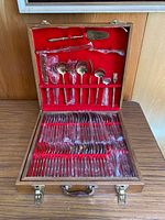 Full view of the open wooden box showing the flatware pieces inside, some wrapped in plastic, secured in red velvet compartments.