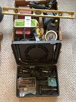 Overview of assorted tools including a wooden level, measuring tape, metal hand tools, and a boxed rotary tool kit.