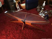 Side perspective of oval glass top coffee table on sculptural wood base