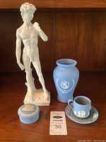 Wide shot of the lot showing the white man statue, blue jasperware vase, teacup with saucer, and trinket box arranged together showing overall condition and size.