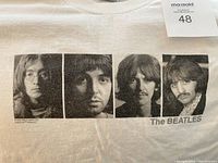 Close-up of black and white individual portraits of the four Beatles members on the front chest area of the white t-shirt, with 'The BEATLES' text below.