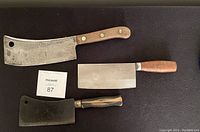 Three meat cleavers with wooden handles laid flat on black surface, all showing signs of wear and use.