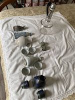 Full overview of the ceramic sake sets and Pyrex coffee urn arranged on a white cloth, showing multiple sake bottles and cups and the tall Pyrex urn with silver bands and lid