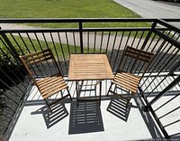 Overall view of teak wood folding bistro set with table and two chairs on balcony floor, showing slatted design and wood tone.
