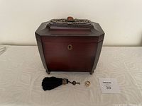 Closed Bombay Company wooden jewelry box with decorative metal top, key with black tassel, gold color costume ring, and MaxSold tag