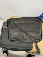 Two black leather courier bags, one stacked on the other showing the front surfaces and shoulder strap.