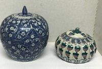 Photo showing two ceramic vases side by side with lids, various floral and geometric patterns.