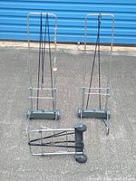 Photo showing three foldable cargo carriers; two upright and one folded on the ground, highlighting their design and wheels.