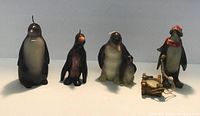 Five decorative penguin candles of various sizes, shapes, and details placed in a row on a flat surface with a plain background.