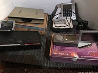 Photo showing multiple electronic items including a beige DVR unit, several phones, a portable radio, and a digital photo frame on a table.