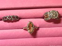 Photo of three rings on pink jewelry display stand showing different stone shapes and settings.