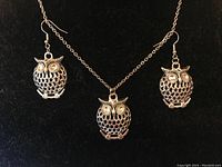 Silver-tone owl pendant on chain with matching owl earrings featuring lattice pattern and yellow eyes.