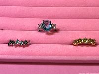 Photo of 3 rings on pink velvet display, showing details of gemstones and band designs