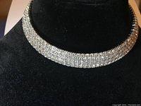 Choker necklace displayed on black velvet jewelry stand, showing multiple rows of rhinestones and clasp closure.