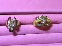 Photo of two gold-colored rings with clear and yellow stones placed in a pink ring holder.