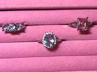 Photo of three rings displayed on pink velvet ring holder, showing all stones and metal detailing clearly