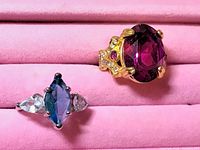 Two decorative rings shown on a pink velvety background, clearly displaying their stones and settings.