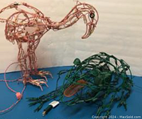 Photo of a pink flamingo and green frog wire sculptures on a blue surface with electric cords visible for motor operation.
