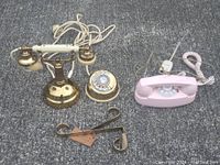 Two rotary dial phones placed on carpet: one brass candlestick style phone and one pink rotary desk phone with pink cord.