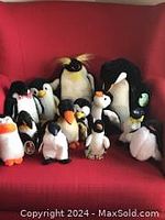 Photo showing twelve stuffed penguin animals of varying sizes and designs placed on red couch.