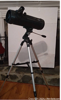 Full view of black reflecting telescope mounted on silver tripod with beige leg supports against white background, showing stability and mounting setup.