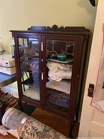 Front view of antique oak and glass cabinet with two glass doors, showing shelves inside containing linens and decorative items.
