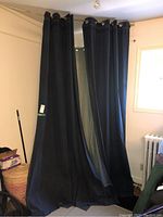 Full view of two dark blue denim curtain panels hung from a rod, showing length and width, hanging style with grommets.