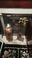 Overall view of the fireplace showing the copper fire extinguisher and the brass fireplace tool set with the horse head design.
