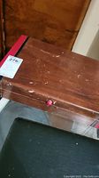 Wooden flatware case closed with scuffs and a red knob on the front