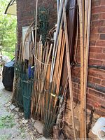 Various wooden stakes, adjustable garden fencing panels, and other gardening items stacked against a brick wall outside.