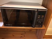 Full view of General Electric microwave oven model JM0426-1 showing front and top with black door and white body.
