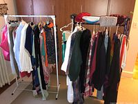 Two clothing racks filled with ladies tops, dresses, skirts, hats, and mittens. Various colors and styles shown, including solid colors and plaids.