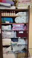 Seven shelves filled with assorted bed linens in different colors and patterns. Seven ceramic spice pots with cork stoppers on the top shelf of a wooden cabinet.