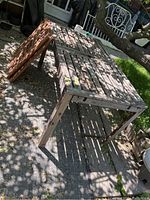 Overview photo of weathered teak outdoor dining table with two side extension panels leaning beside it outdoors.