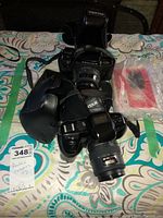 Two black Pentax cameras with attached lenses, leather cases and straps displayed on patterned fabric.