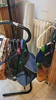 Front view of the black metal rack holding several bags including a blue backpack and brown purse.