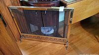 Front view of the brass fire screen showing mesh curtains with decorative brass frame and feet
