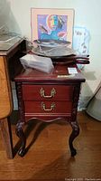 Front view of dark mahogany side table with two drawers and brass handles, carved legs visible