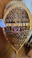 Full view of the vintage snowshoes showing formed wood frames, sinew webbing, and leather bindings.
