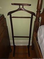 Full view of wooden suit hanger stand next to furniture and bed showing overall structure.