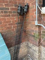 Two tall black metal garden oil torches leaning against a brick wall, showing wear.