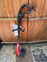 Full view of the Toro garden trimmer leaning against a wooden fence, showing the black and red body and blade guard.