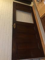 Full view of a vintage solid oak door with three lower panels and a missing upper glass insert, showing original brass hardware and the door's dark wood finish.