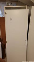 White Ikea wardrobe cabinet standing upright with the door detached and leaning against the wall. Shows overall shape and door condition with some missing screw holes.